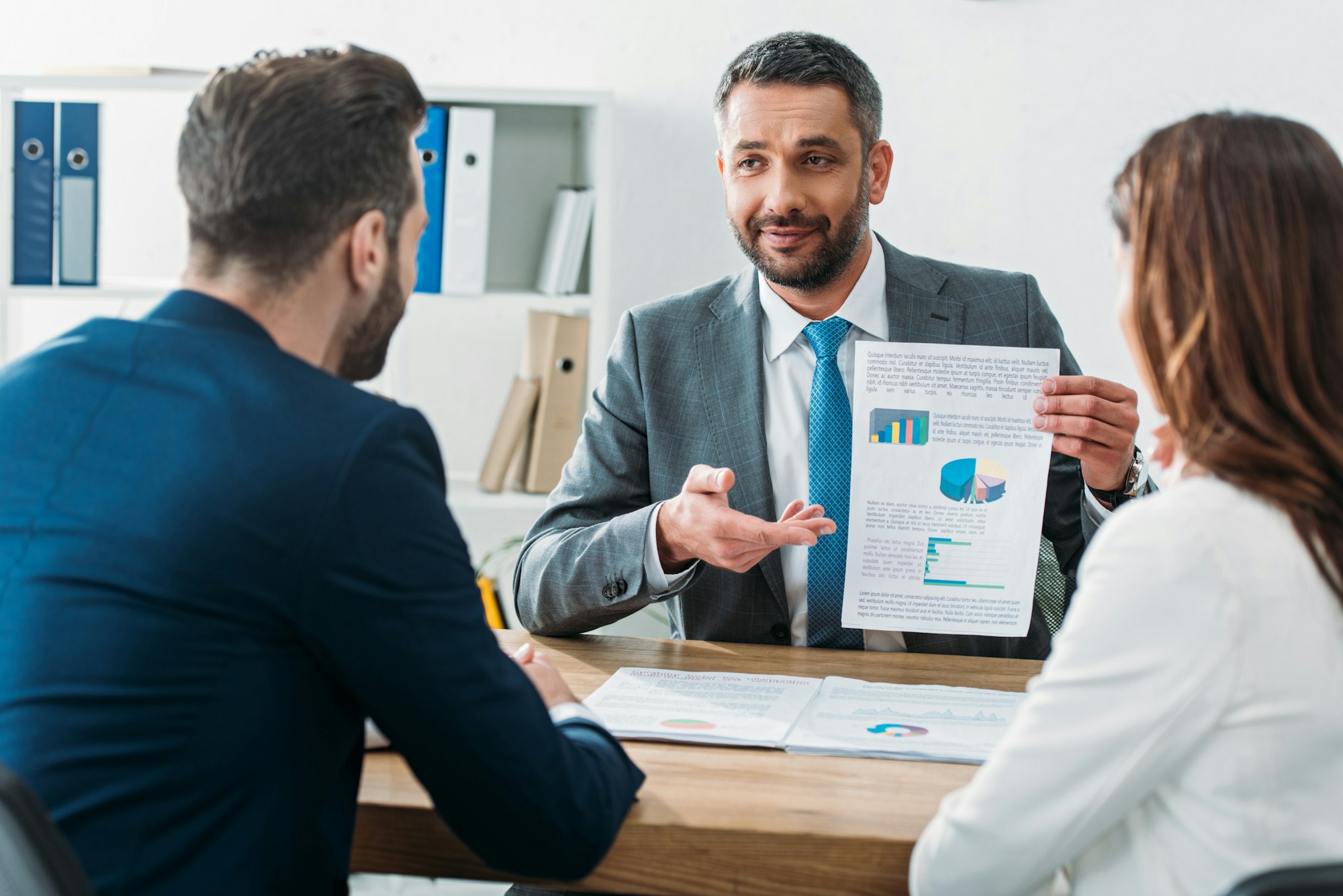 selective focus of handsome advisor showing document to investors at workplace