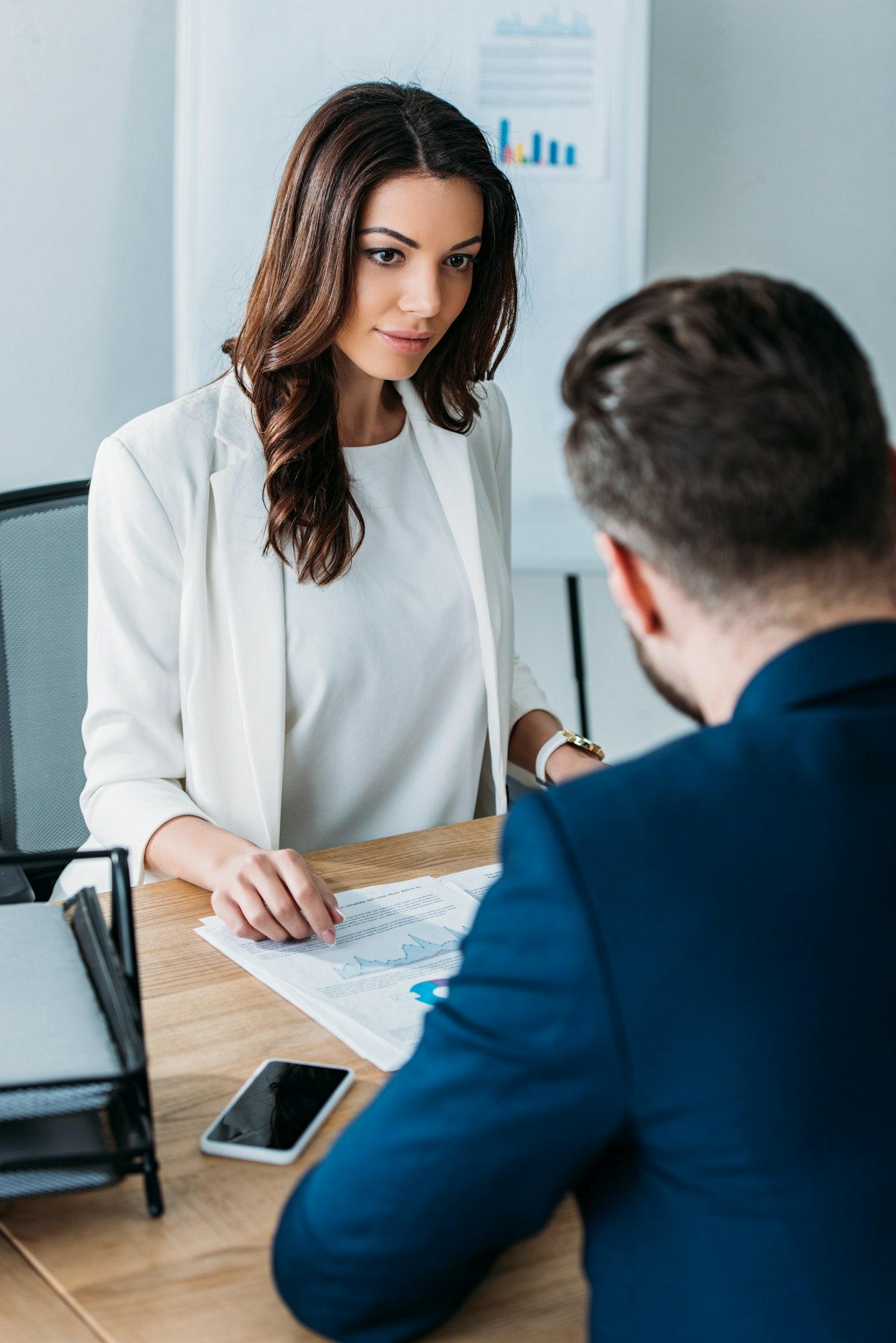selective focus of attractive advisor and investor in suits discussing document at office